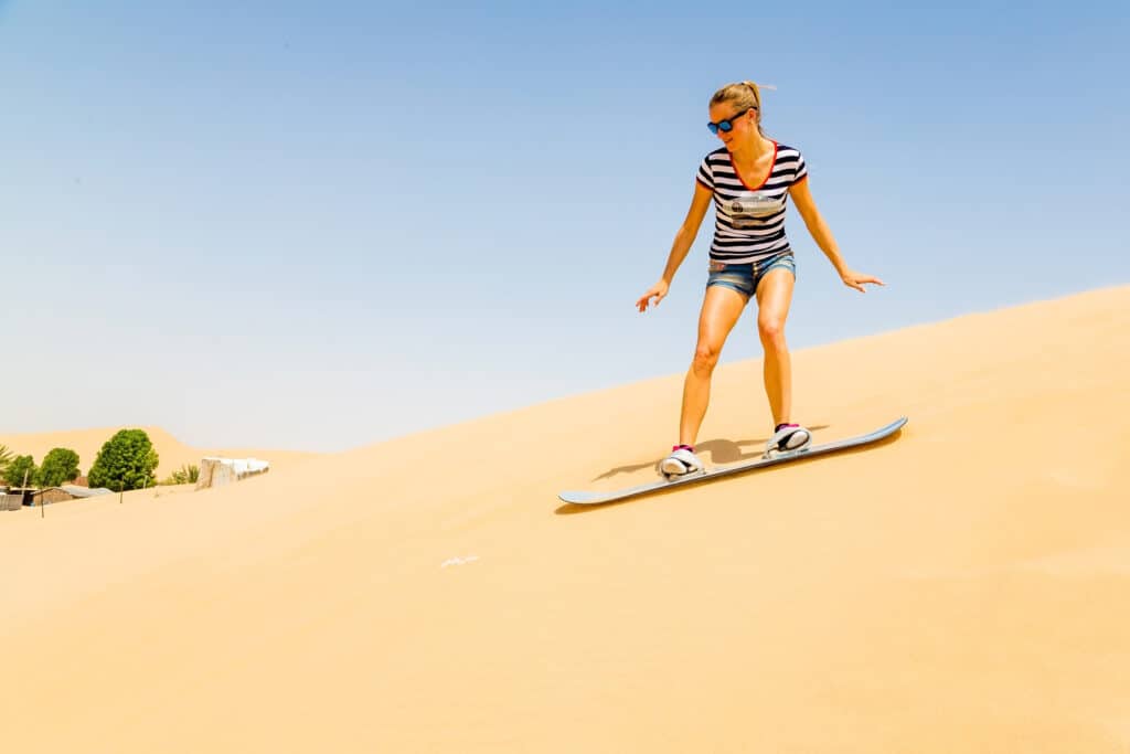 kvinde på sandboard på vej ned af en bakke af sand i økenen i dubai